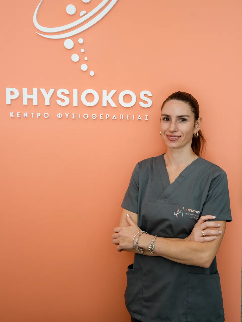 Η φυσικοθεραπεύτρια Ζωή χαμογελαστή στον κοραλί τοίχο του PhysioKos